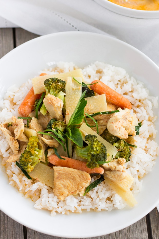 Overhead view of a white bowl with rice and red curry with chicken and vegetables on top.