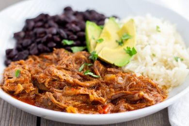 White bowl with pot roast on one half, white rice and black beans on the other half. Topped with Avocado slices.