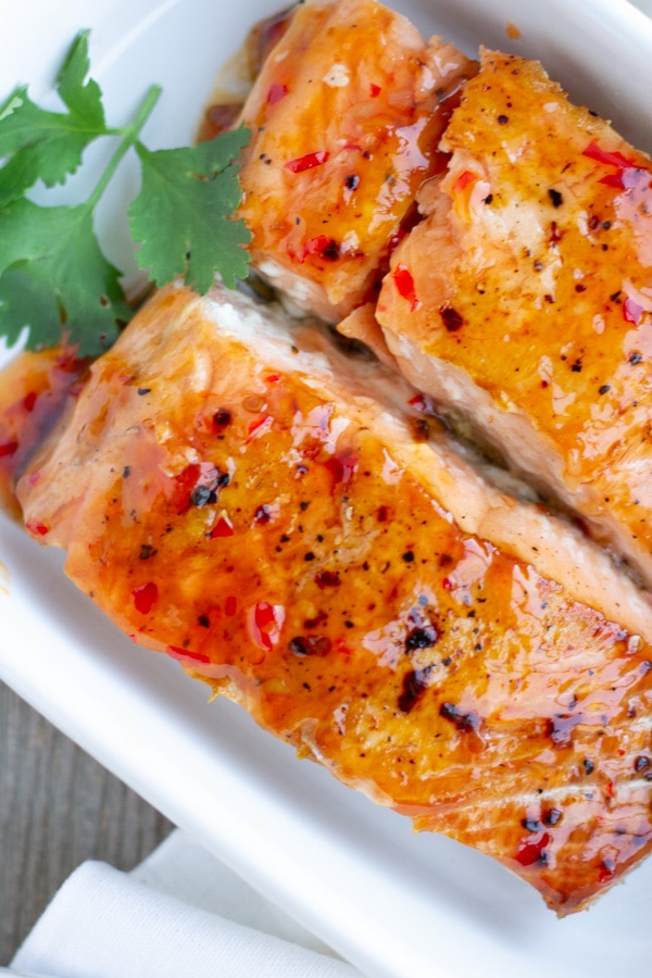 Up close view of 2 salmon fillets with sweet chili sauce in a white baking dish.