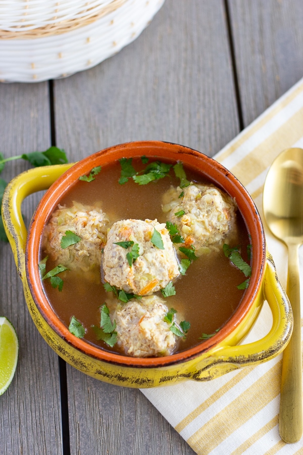 Meatball soup in a yellow bowl. With a gold spoon on the side.