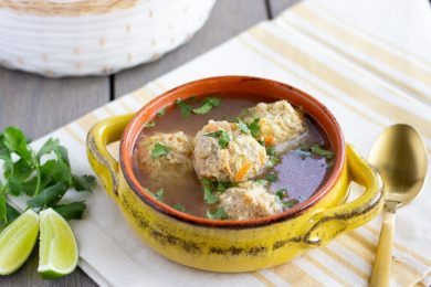 Albondigas in a yellow bowl with a stripped yellow napking underneath.
