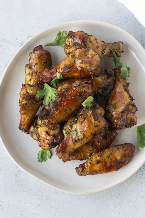 Overhead view of wings on a round white plate topped with cilantro.