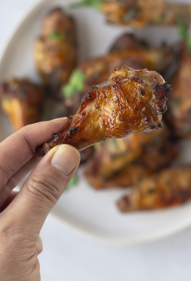 Hand holding a drum over the plate of wings.