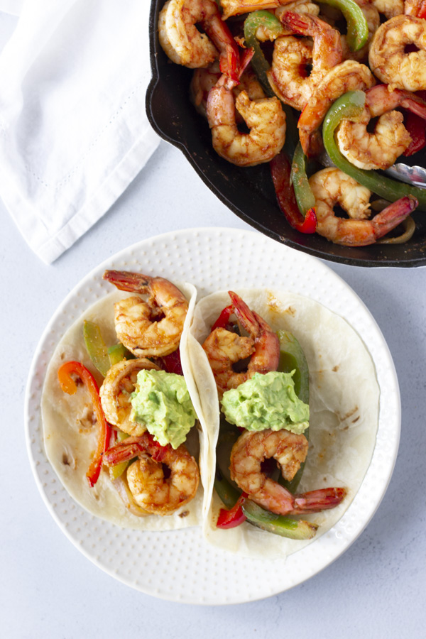 Two shrimp tacos on a plate with a skillet in the back