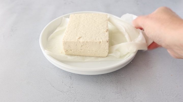 Block of tofu on a plate with paper towels.