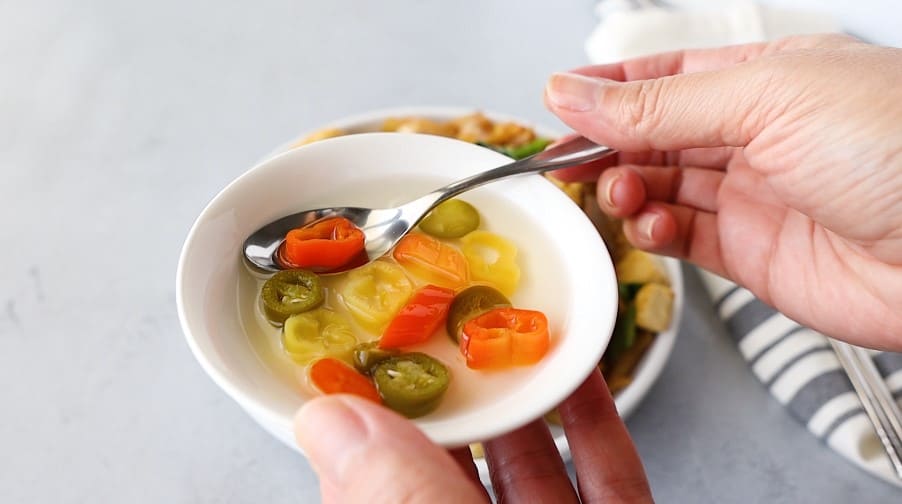 Small white bowl with vinegar and sliced jalapenos.