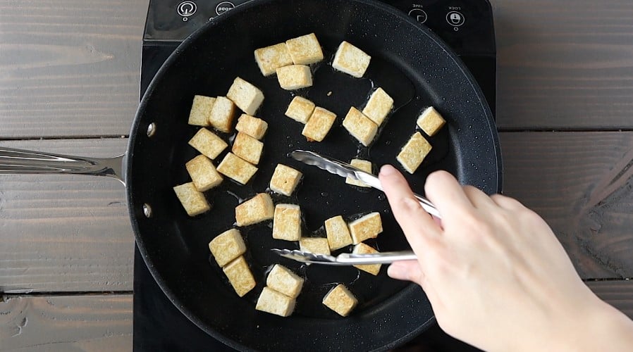 Tofu cubes in a skillet being fried.