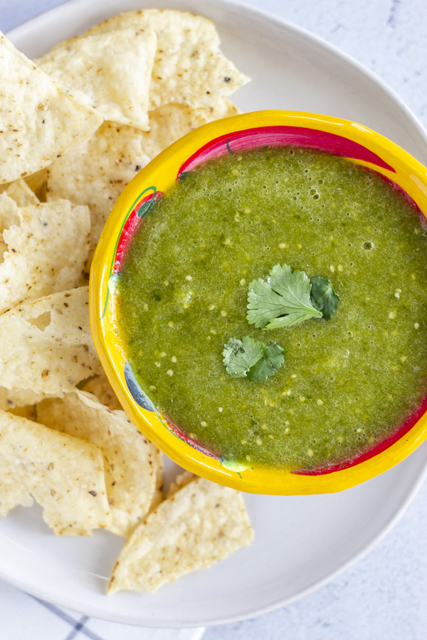 Overhead view of salsa verde in a bowl on a plate with chips.