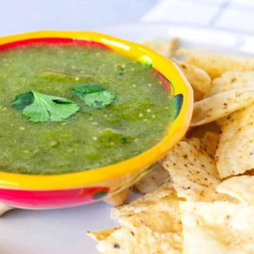 Up close view of salsa verde in a yellow bowl with tortilla chips on the side.
