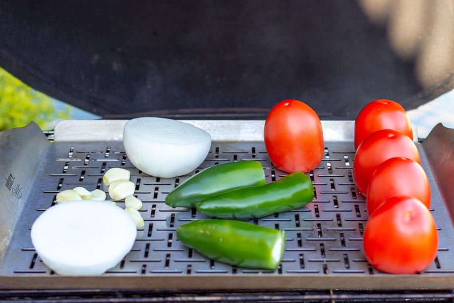 Tomatoes, jalapenos, onions, and garlic on a grill grate for roasting.