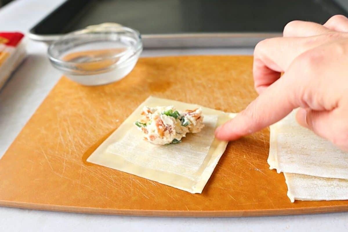 Hand folding a wonton wrapper with filling in the middle.
