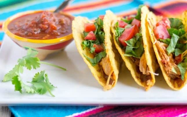 3 tacos on a white plate under a colorful Mexican placemat.