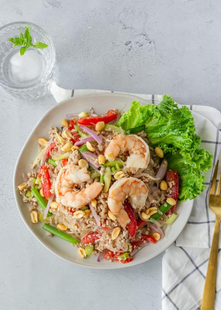 Overhead view of glass noodle salad with a gold fork and glass of water.