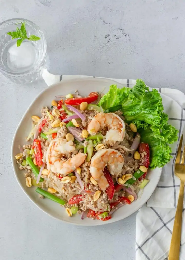 Overhead view of glass noodle salad with a gold fork and glass of water.