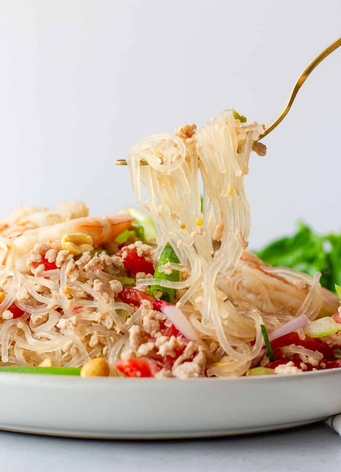 Fork holding clear noodles over plate.