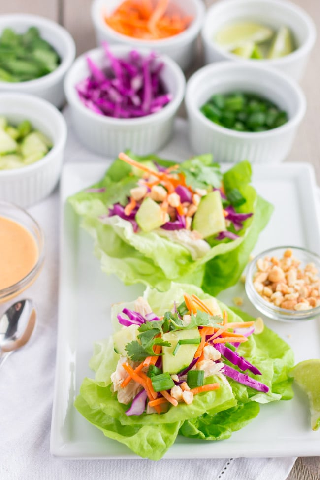2 lettuce wraps on a plate with toppings in small bowls. 
