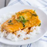 Small white plate with white rice on the bottom and a piece of red curry cod on top.