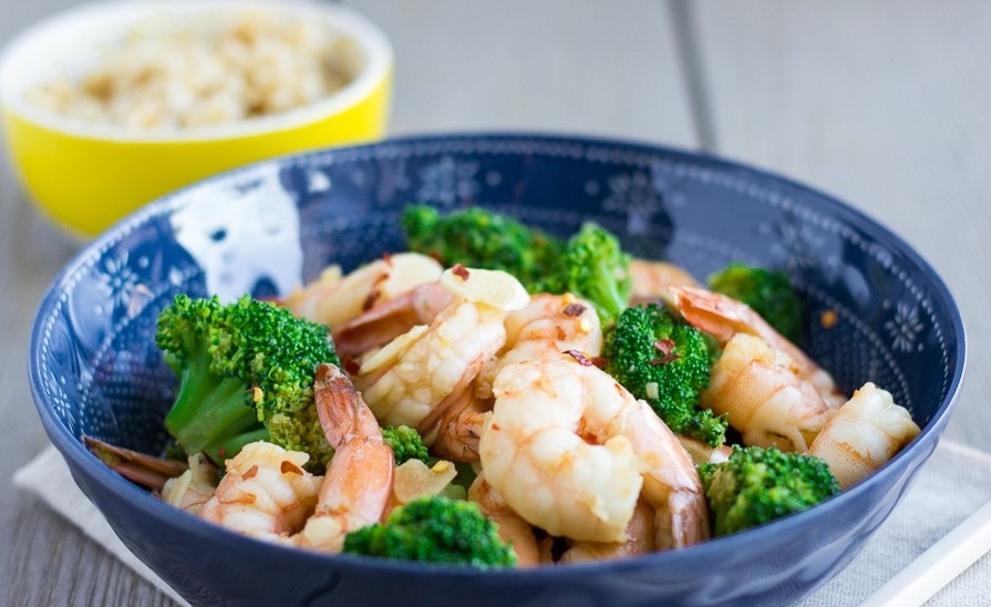 Landscape view of shrimp and broccoli stir fry with a small yellow bowl in the back.