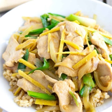 Up close view of stir fry with ginger, chicken and green onion slices.
