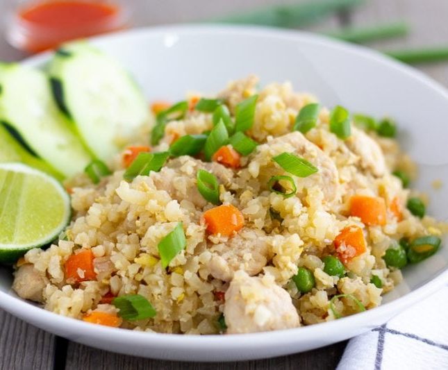 Thai Cauliflower Fried Rice in a white bowl with a lime wedge and cucumber slices on the side.