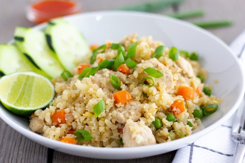 Thai Cauliflower Fried Rice in a white bowl with a lime wedge and cucumber slices on the side.