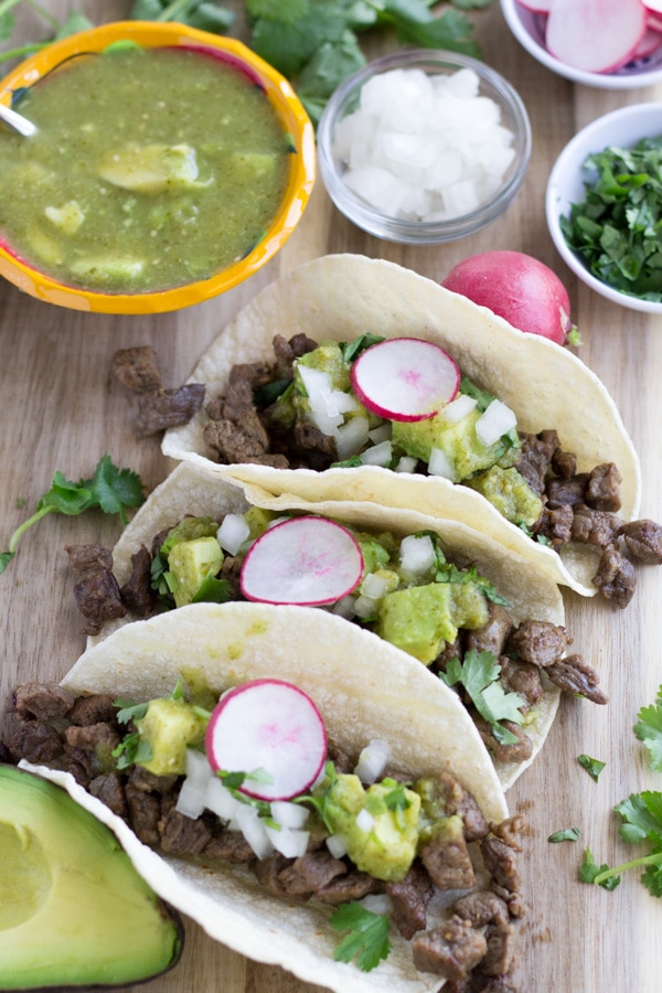 3 Tacos on a wood cutting board with toppings.