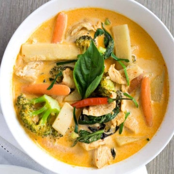 Overhead view of red curry in a white bowl with bamboo shoots, carrots, chicken, and broccoli.