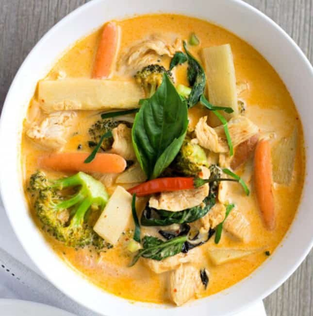 Overhead view of red curry in a white bowl with bamboo shoots, carrots, chicken, and broccoli.