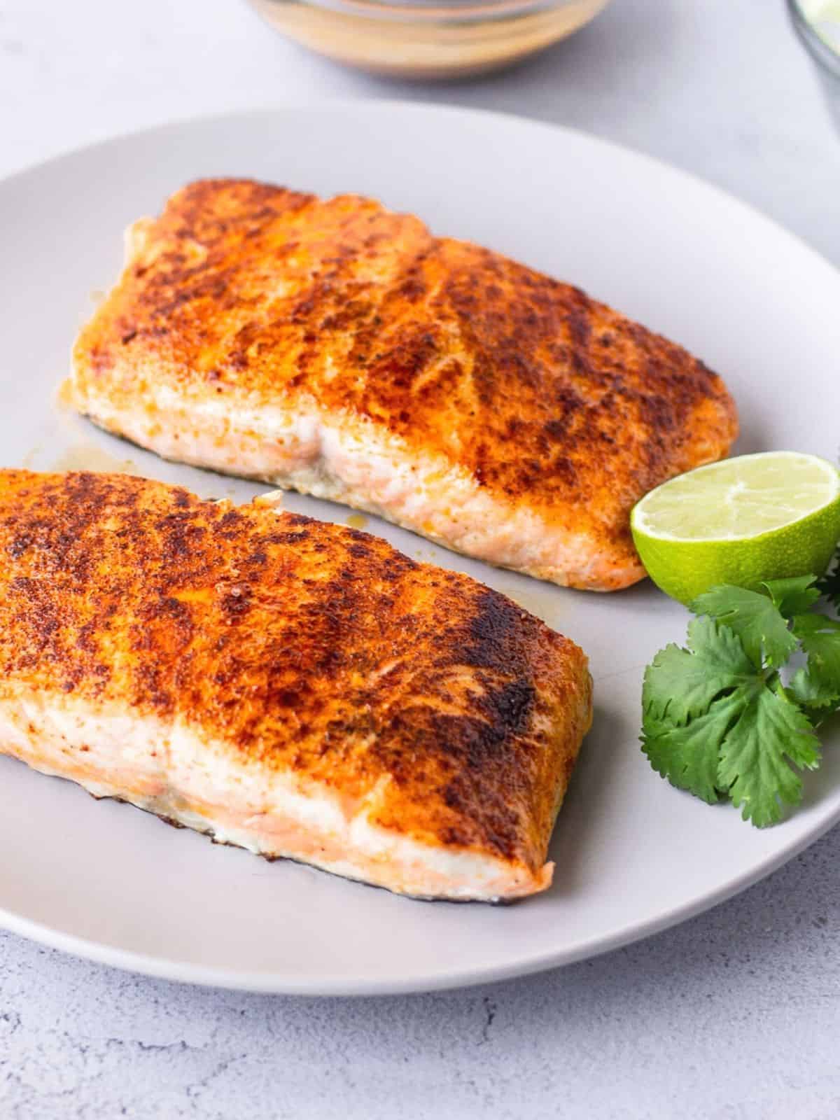 Two pieces of cooked salmon filets on a white plate.