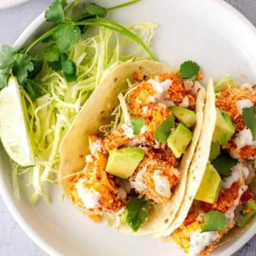 2 Tacos on a plate with a side of cabbage and cilantro.