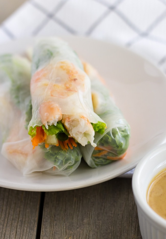 Three rice paper rolls on a plate with a bite in the top one.