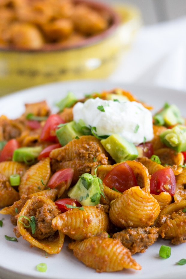 Up close view of small pasta shells, ground beef, diced avocado, tomato, and sour cream on top.