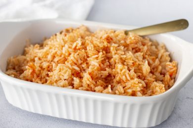 Rice in a white dish with a gold spoon and white napkin on the side.