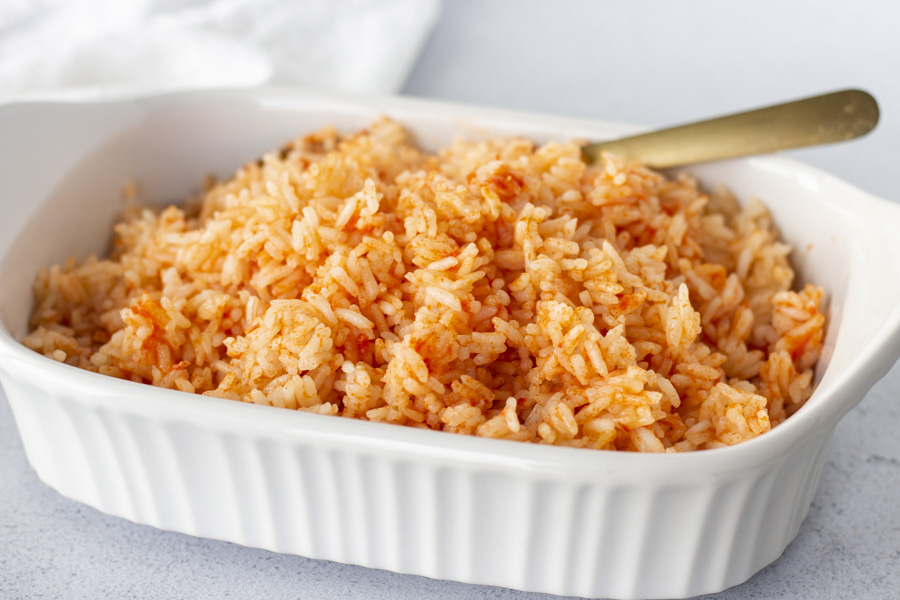 Mexican red rice in a white dish with a gold spoon and white napkin on the side. 