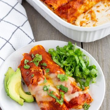 Enchiladas on a plate with a side of avocado and lettuce.