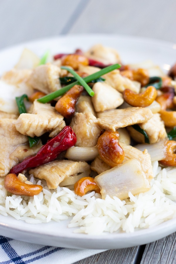 Cashew chicken over rice on a white plate.