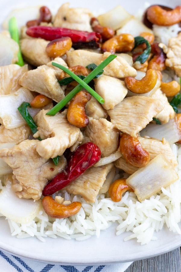 Up close view of cashew chicken over rice on a white plate. 
