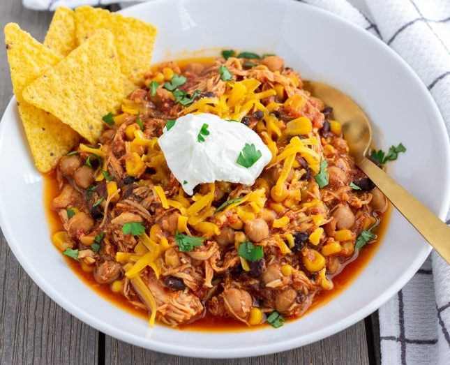 Landscape view of Chicken Taco Chili in a white bowl with a dollop of greek yogurt in the middle and tortilla chips on the side