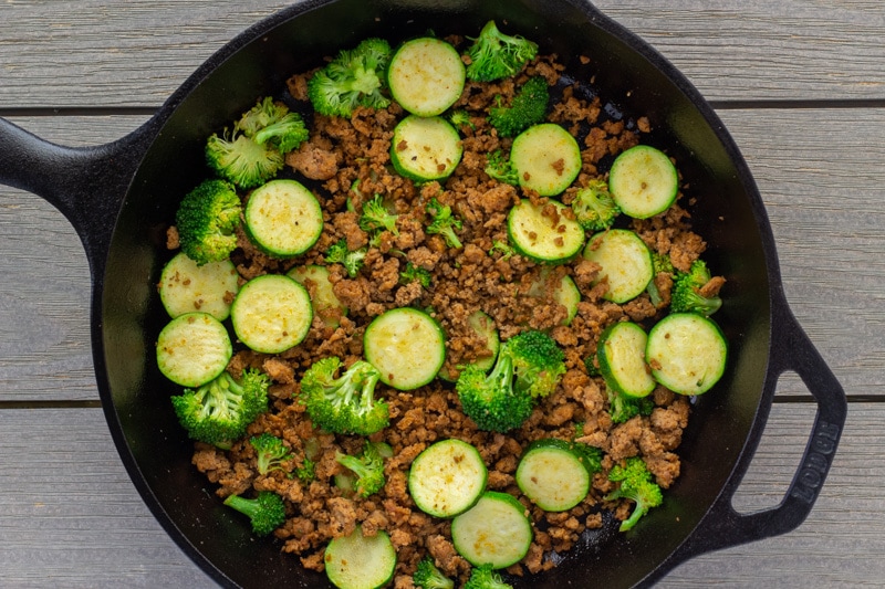 Cooked ground turkey, sliced zucchini, and broccoli florets in a cast iron skillet.
