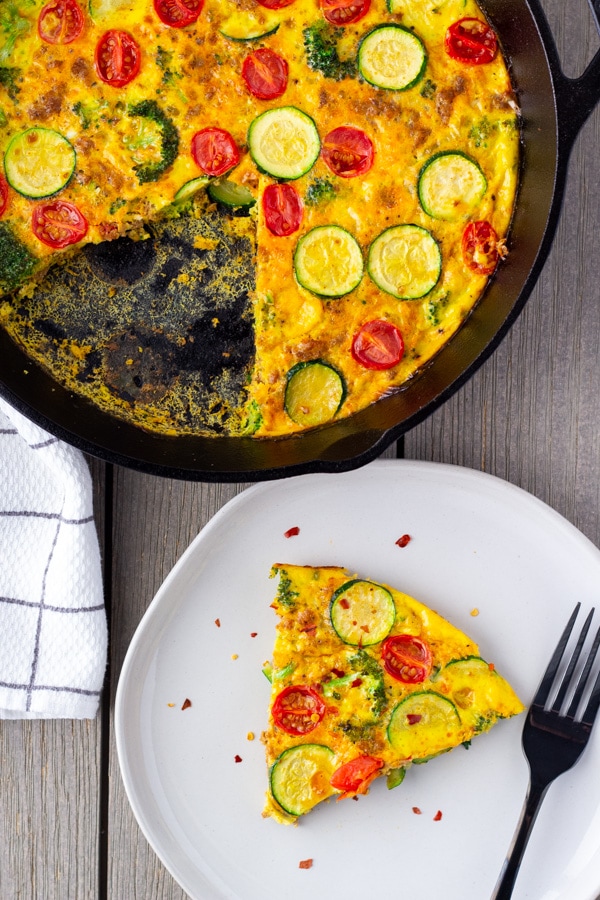 Slice of frittata on a plate with the whole one in a cast iron skillet on the side.