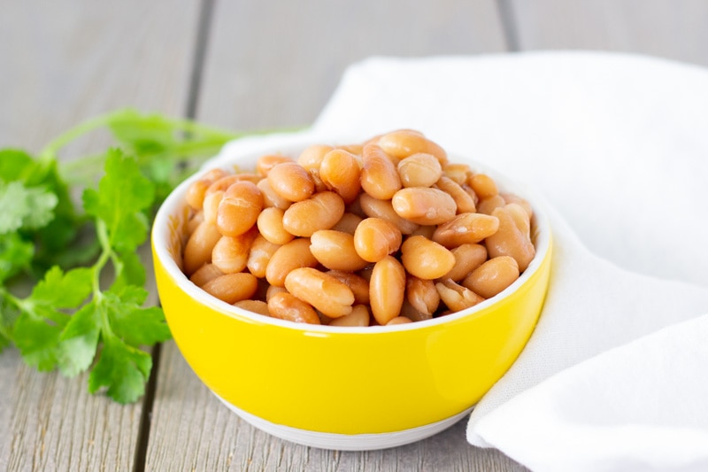 Cooked Peruvian beans in a small yellow bowl with cilantro on the side.