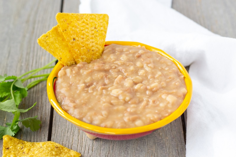 Refried Peruvian beans in a small yellow bowl with tortilla chips on the side.