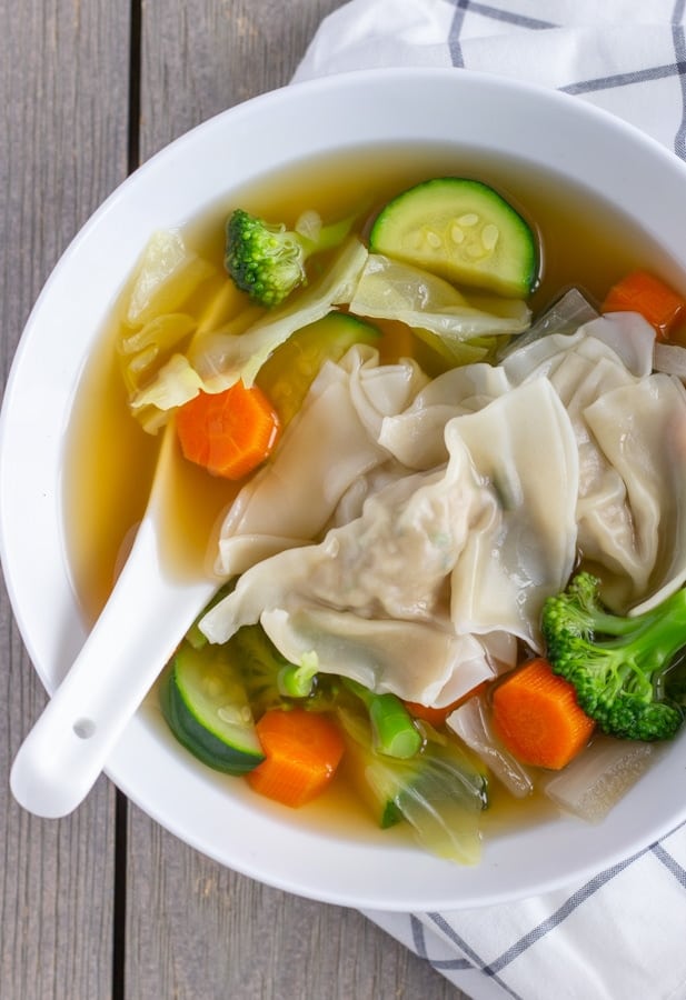 Wonton and Vegetables in a white bowl with a white soup spoon inside.
