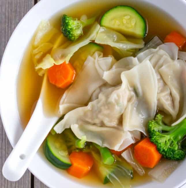 Wonton vegetable soup in a white bowl with a white soup spoon.