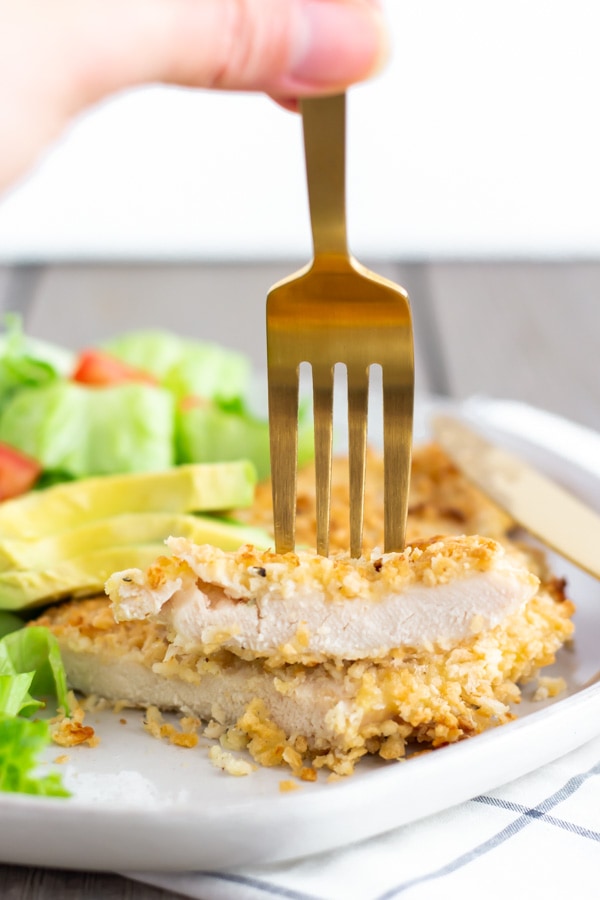 Chicken milanesa cut in half and stacked with a fork on top.