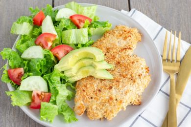 Chicken milanesa on a white plate with a side salad.