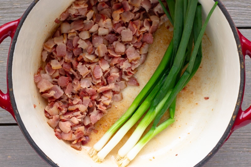 Dutch oven pot with cooked bacon on one side and whole green onions on the other side.