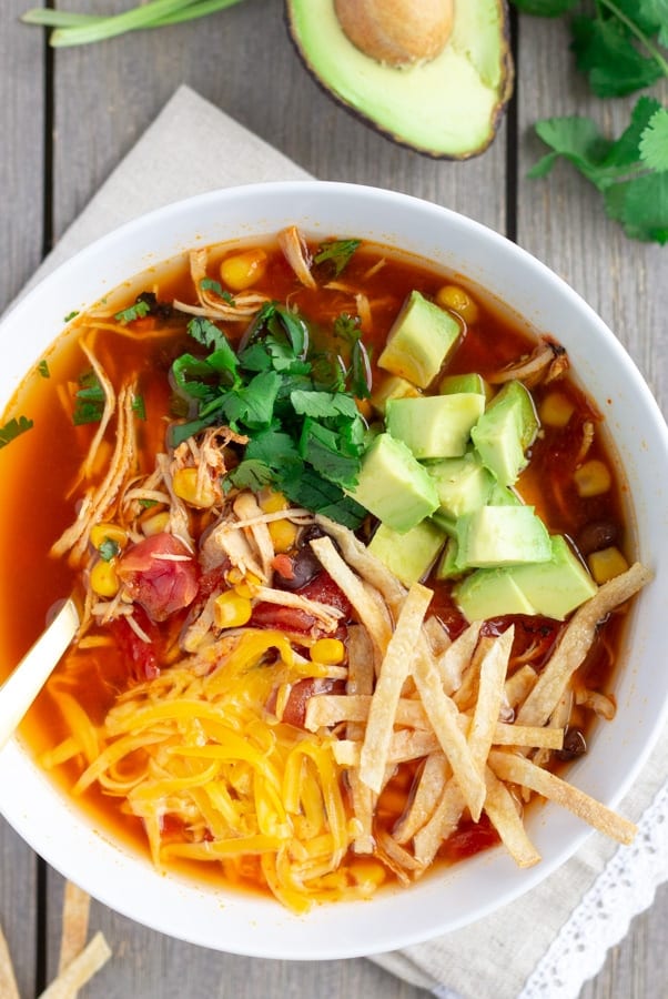 Overhead view of chicken tortilla soup in a white bowl with half an avocado and cilantro leaves on the side.