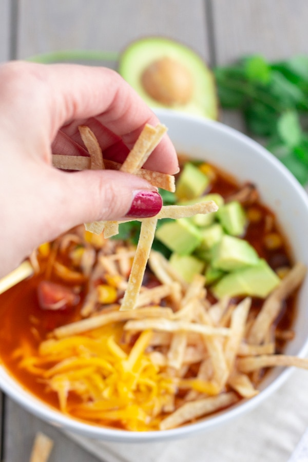 Hand shot of tortilla strips being sprinkled into chicken tortilla soup