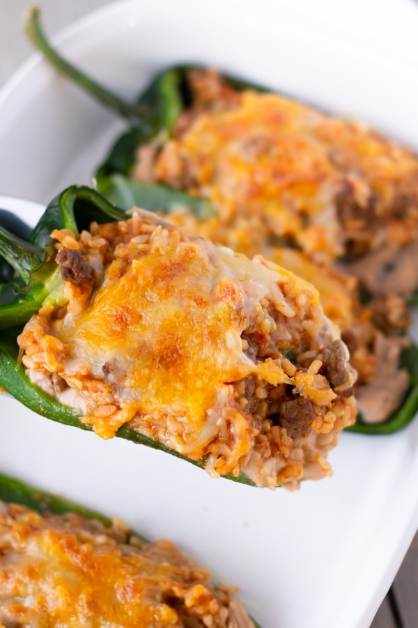 Cooked stuffed poblanos in a white baking dish with a close up of one being served.